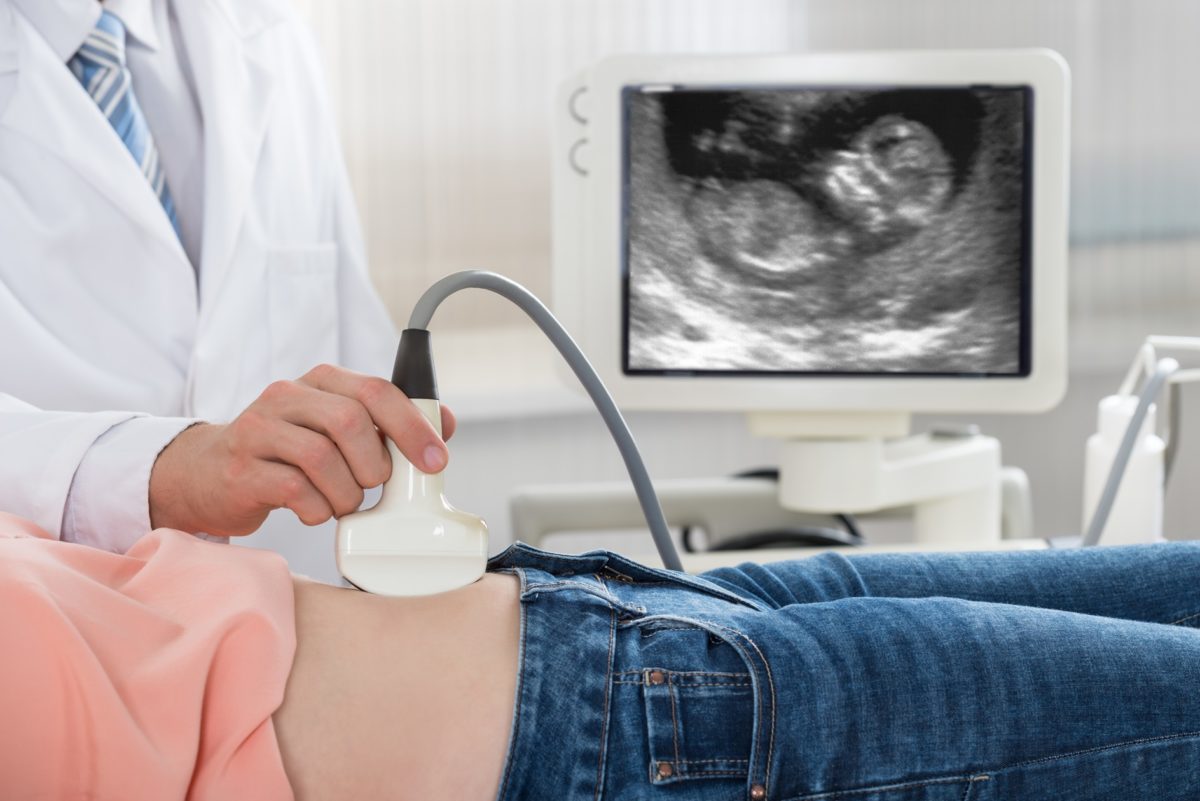 Cropped image of male doctor moving ultrasound probe on pregnant woman's belly